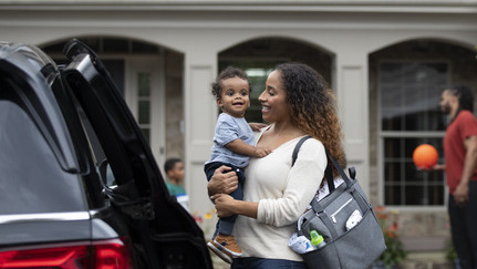 Woman with diaper bag holding her baby outside of her vehicle