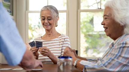 Happy seniors sit at a table playing card games