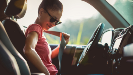 A teen driver buckles her seatbelt.