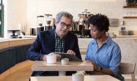 A woman and a man at a coffee shop having a meeting while holding a tablet.