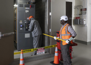 Worker in arc flash suit racking a new breaker with a site supervisor spotting the installation