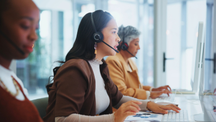 Three women with headsets working on computers.