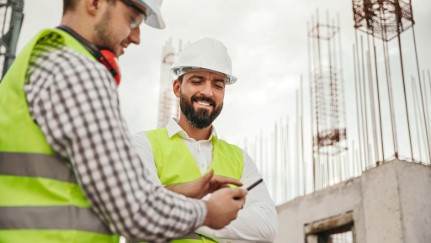 Two construction workers look at a smartphone.