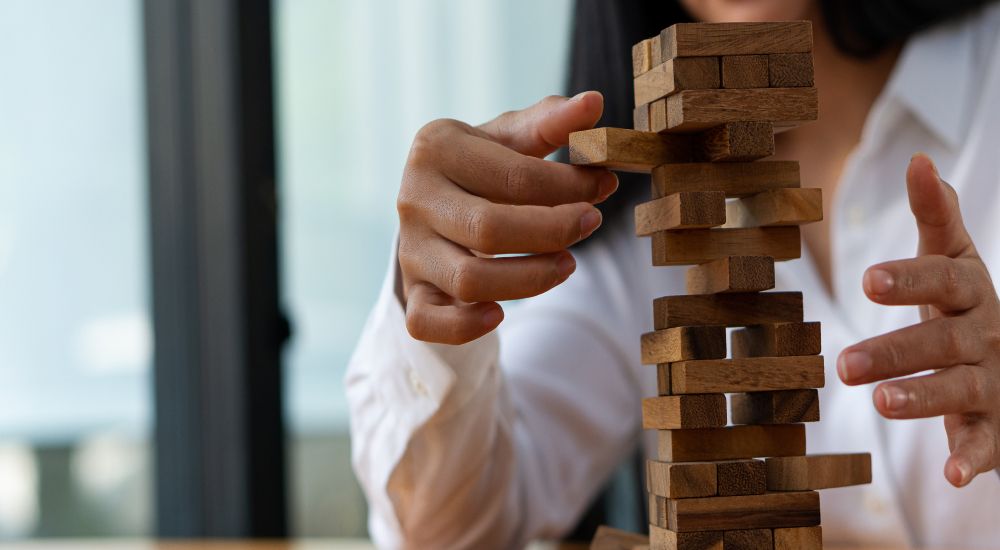 A person in a white shirt carefully removes a wooden block from a tall, unstable stacking tower game.