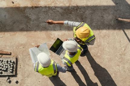 Three workers in hard hats reviewing documents on construction site.
