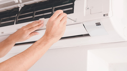 A person performs maintenance on their air conditioner with a screwdriver.