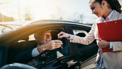 A saleswoman hands a customer the keys to a new car.
