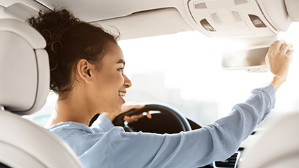 A woman checking the rearview mirror of her car.