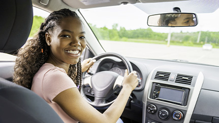 conductor adolescente sonriente sentado detrás del volante de un auto