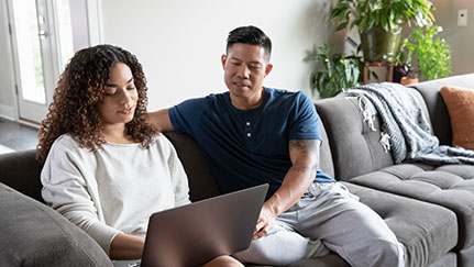 man and woman sitting on a couch looking at a laptop