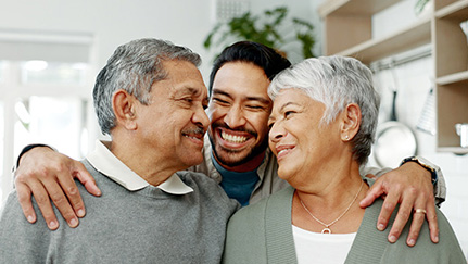 Smiling adult child standing between two older adults, arms around their shoulders