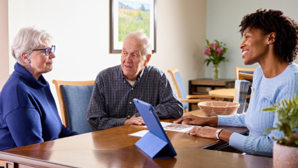 A financial professional meets with an older couple at a table, to review documents together.