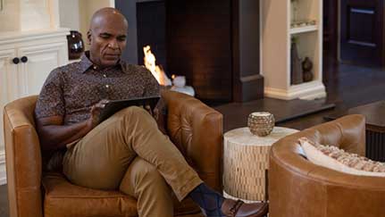 man reading from digital device while sitting by a fireplace