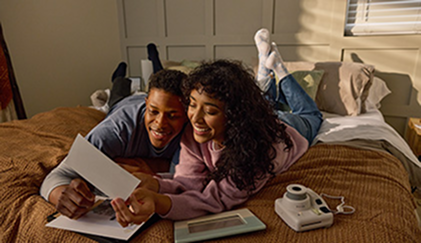 A couple lying on a bed, smiling and looking at a photo while holding it together.