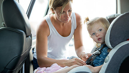 Mother putting a toddler into a car seat in a family car
