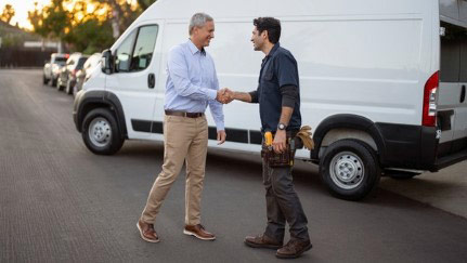 Two men shaking hands in front of commercial vehicle