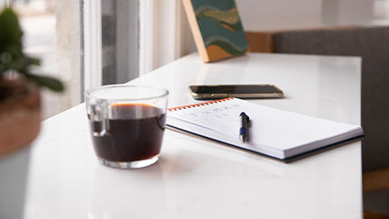 desk with cup of coffee, pad of paper, and cell phone