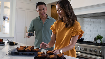a husband and wife baking muffins together in their kitchen