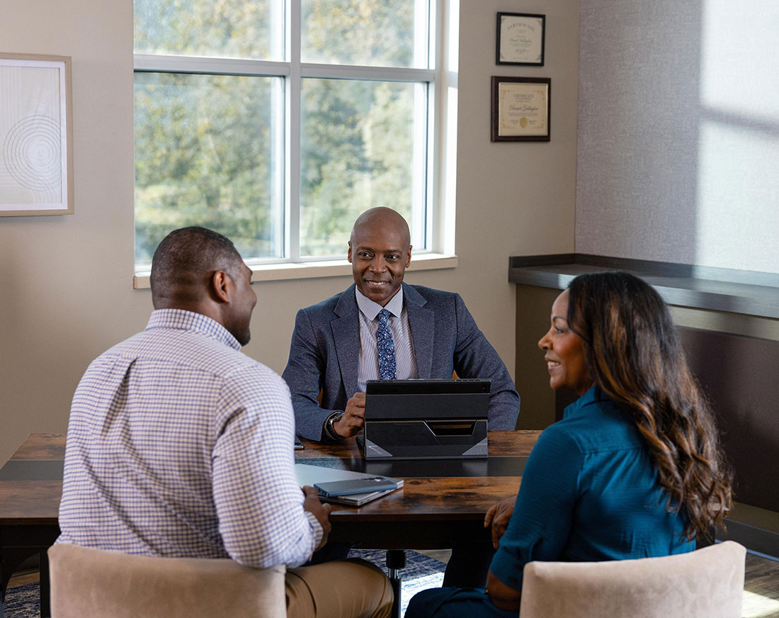 A middle aged married couple meets with their financial professional in his office to discuss long-term care solutions.
