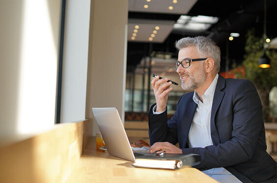 Man sitting in a coffee shop on a laptop talking on the phone and working.