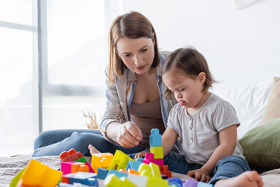 A child with special needs plays with colorful toy blocks on a bed with their mother.