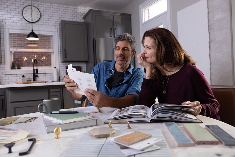 A married couple compares paint swatches while sitting at their kitchen table.
