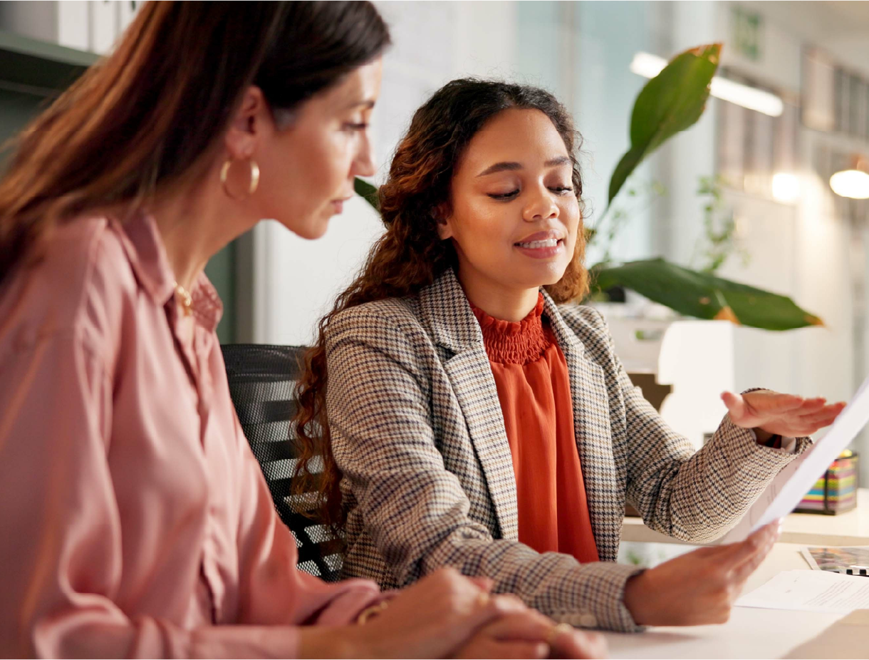 2 women sitting at a table and looking over a document