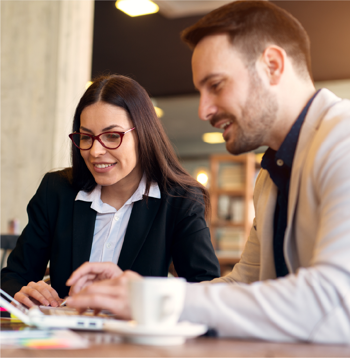 man and woman sitting at a café looking at a laptop