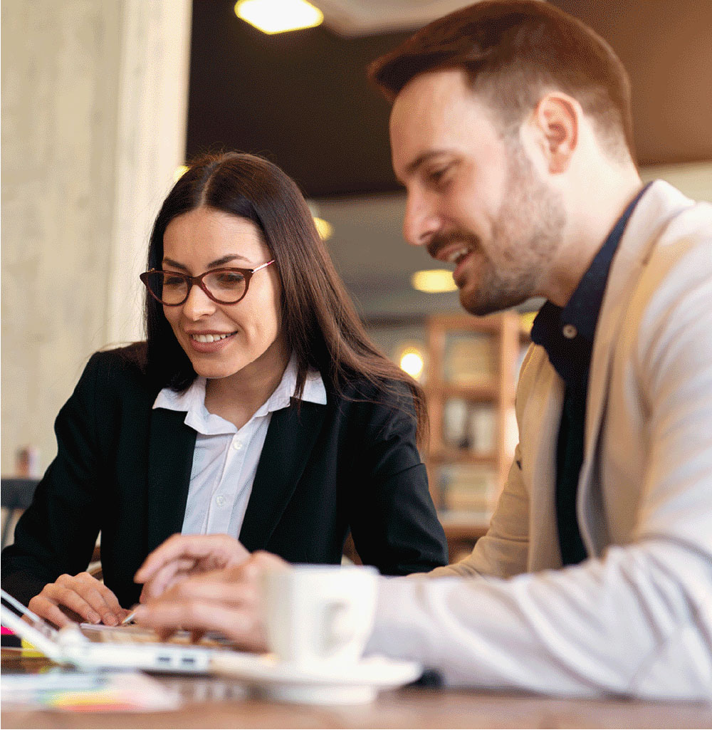man and woman sitting at a café looking at a laptop