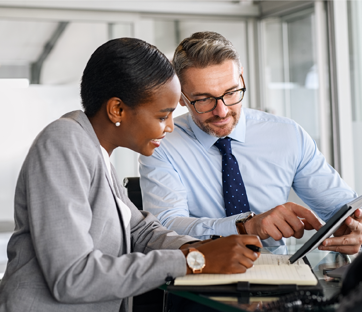 Two people in an office setting working and looking at a tablet together. 