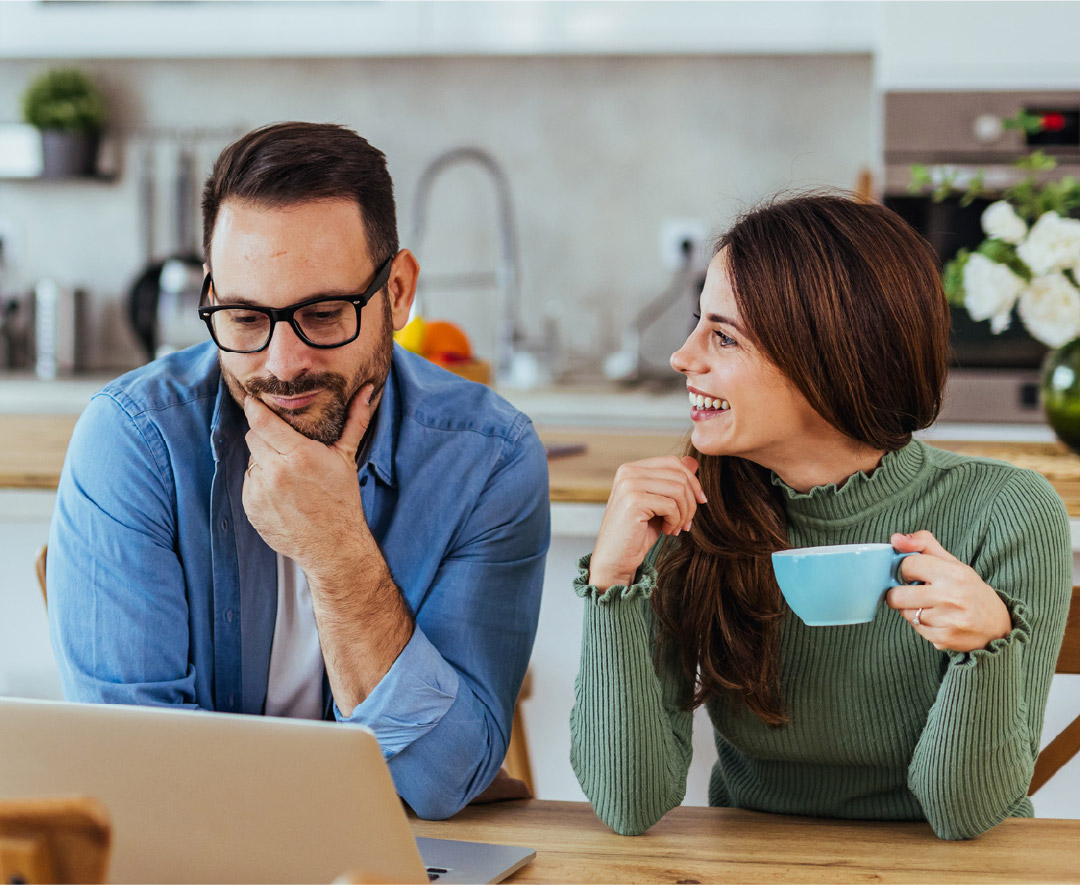 Man and woman sitting down at a table, looking at a laptop.