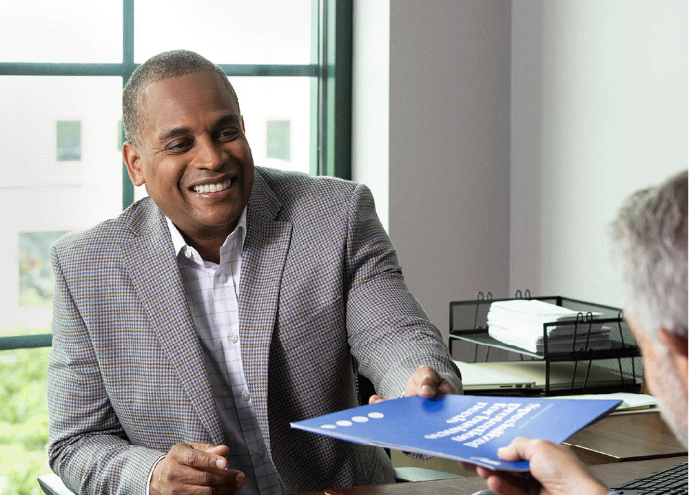 Man in his 60s meeting with a financial professional and getting a document handed to him.
