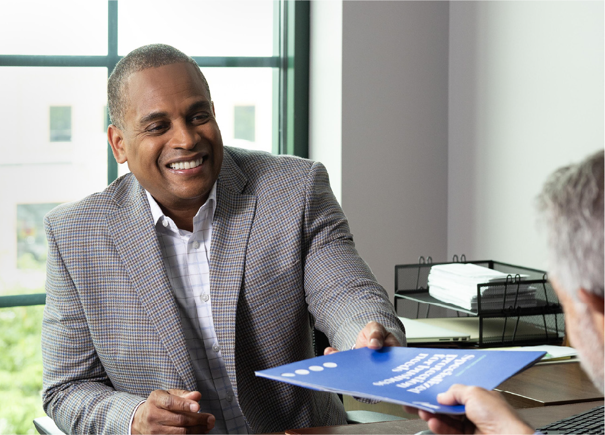 Man in his 60s meeting with a financial professional and getting a document handed to him.