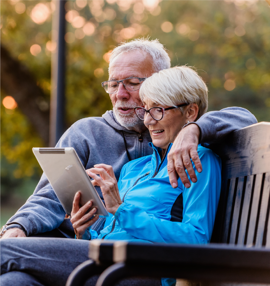 couple in their 70s sitting outside and looking at a tablet.