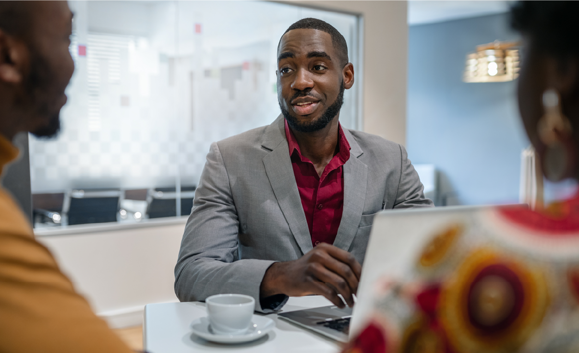 Man sitting at a desk with his computer and talking to two people.