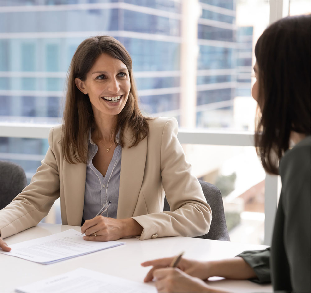 2 women talking while sitting at a desk in an office