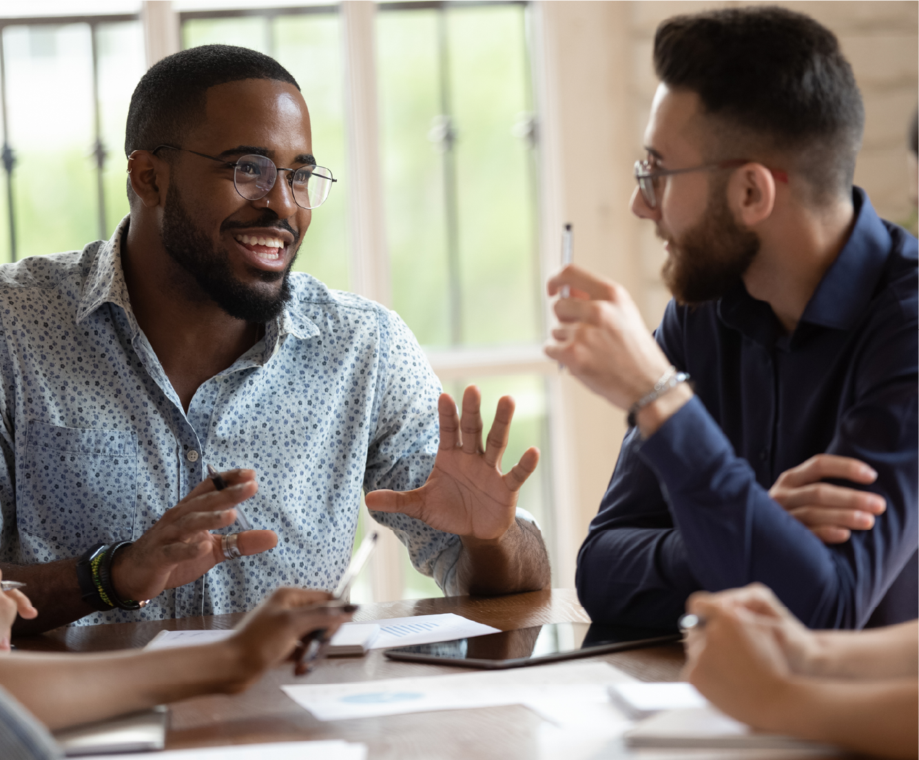 Two male coworkers sitting at a table talking and smiling.