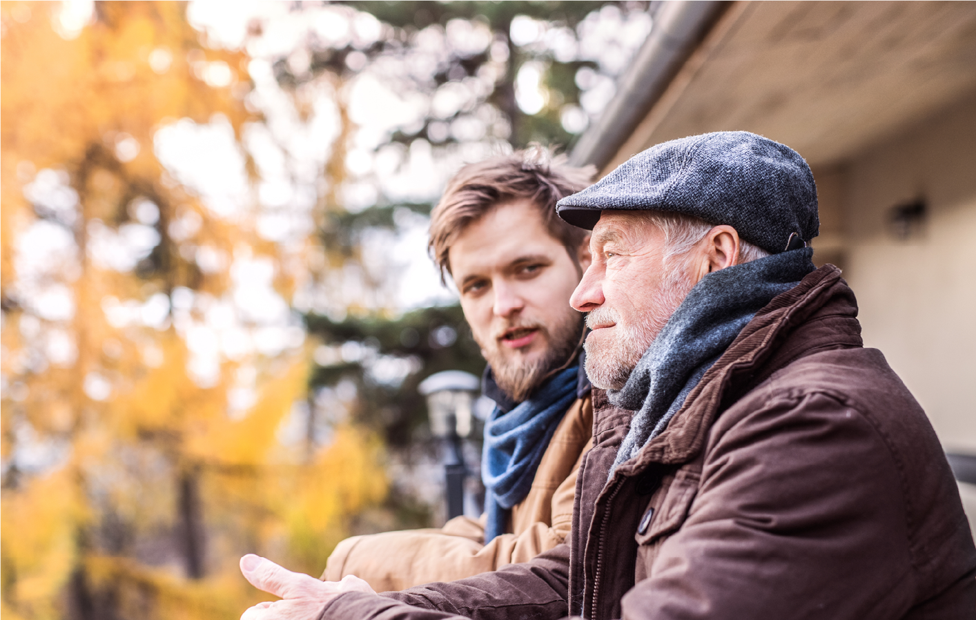 Older and younger man sitting down outside in the fall and talking.