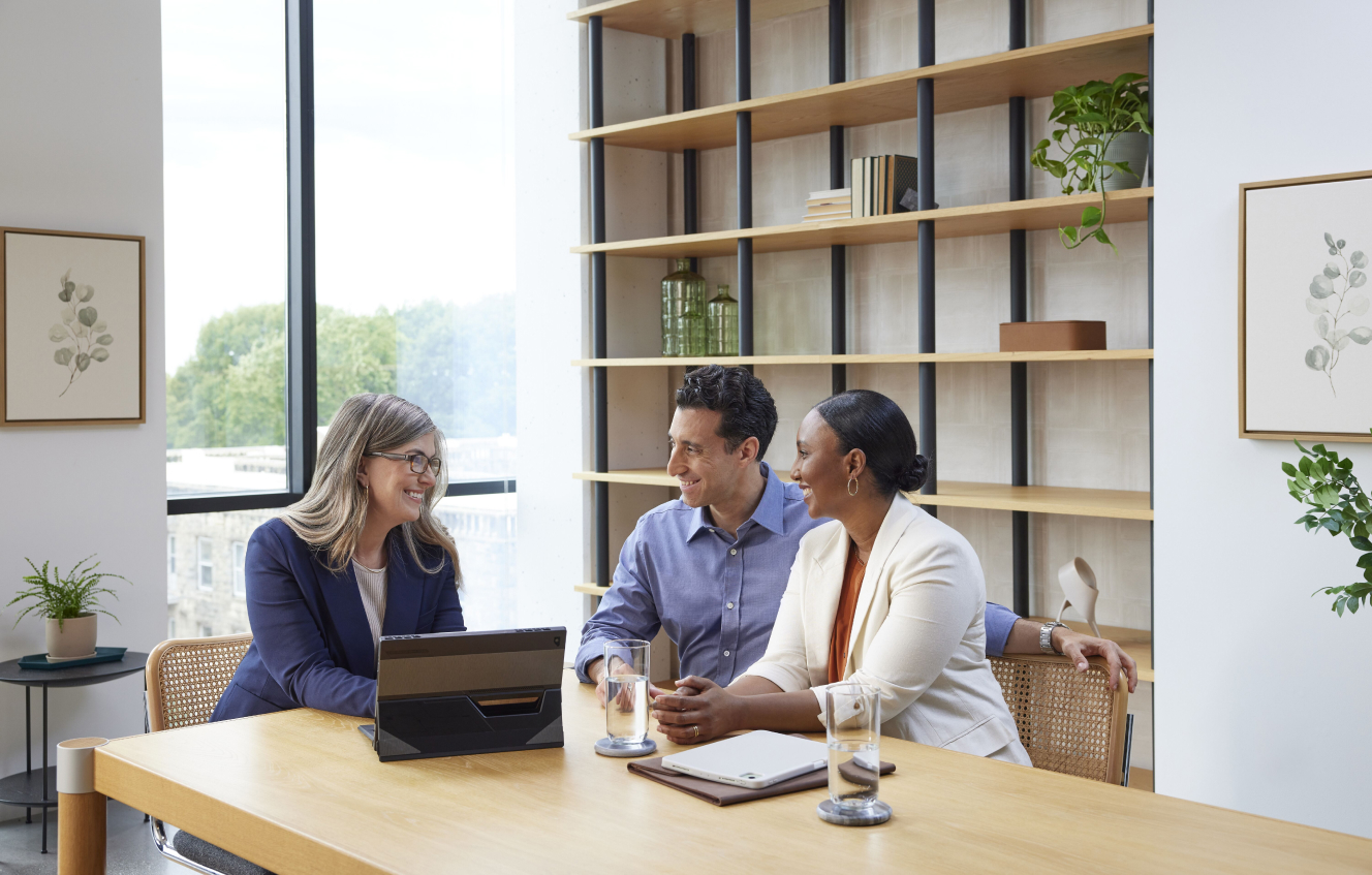a financial advisor with a laptop in front of her sitting at a table talking to a man and woman