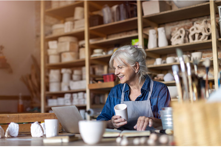 A pottery maker inspects a mug while managing their small business online.
