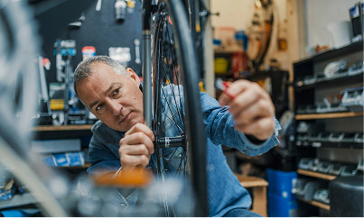 An employee repairing a bicycle wheel in a well-equipped workshop, adjusting spokes with precision amid organized tools and parts