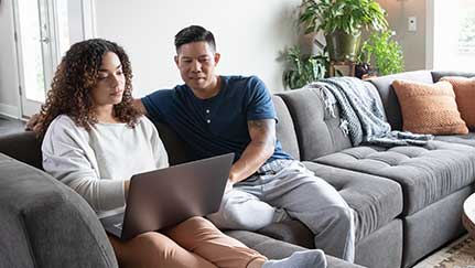 couple sitting on couch looking at a laptop
