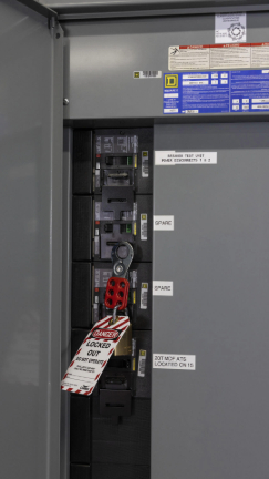 Close-up photo of an open electrical box with a lockout tag locked to an electrical control