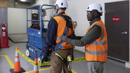 Construction supervisor inspecting worker fall protection harness.