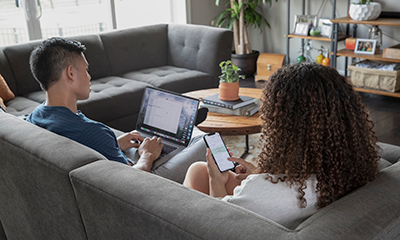 man and woman sitting on a couch and using a laptop and phone