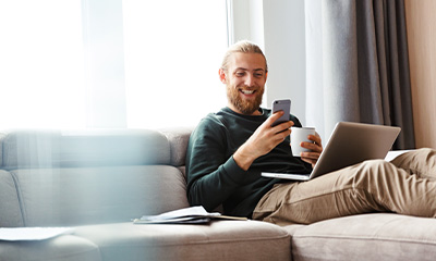 man and woman sitting on a couch and using a laptop and phone