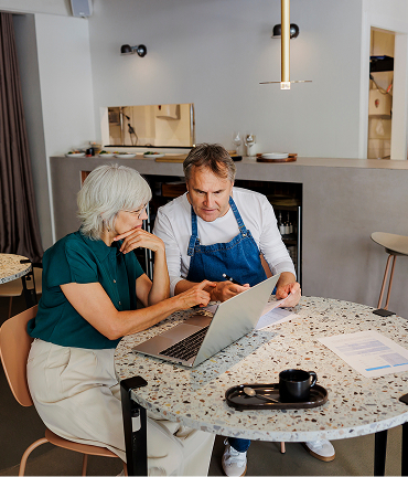 A financial advisor and a shop owner discuss business over a laptop in a café.
