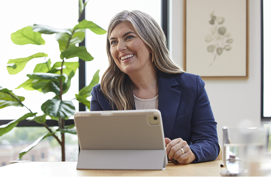 Woman sitting at desk with a tablet smiling off screen