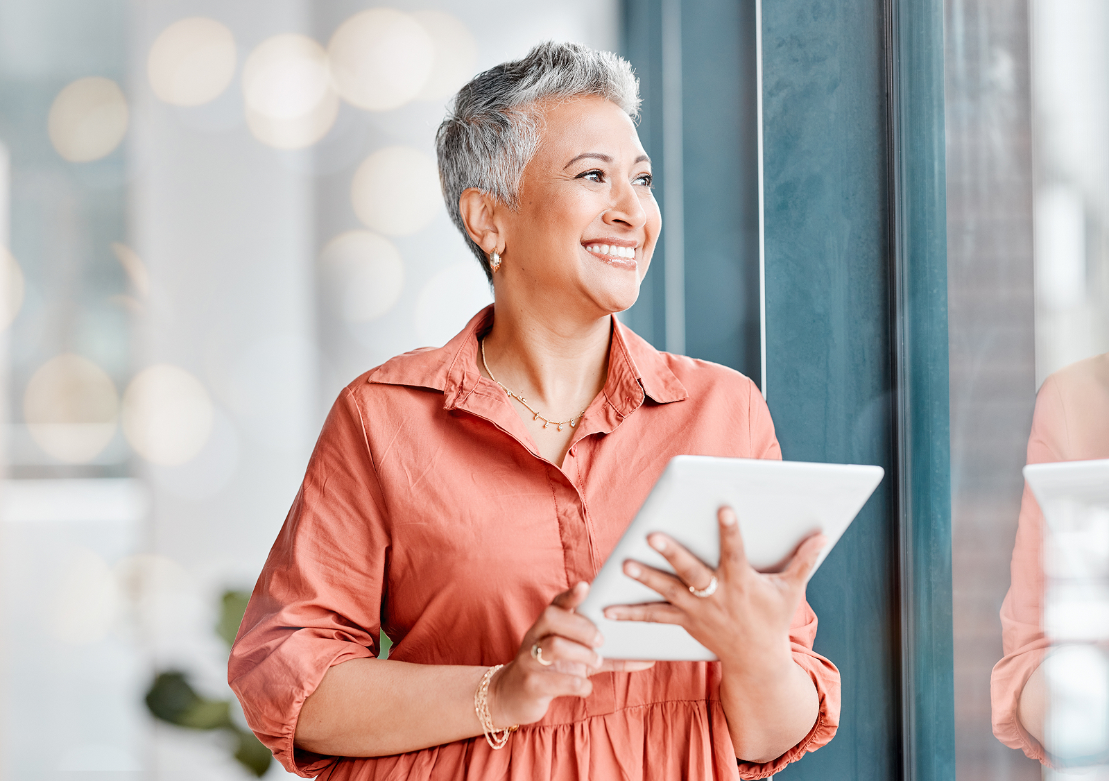 A smiling person holds a tablet near a sunlit small-business shop window.