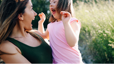 A woman holding a young girl with down syndrome outdoors.